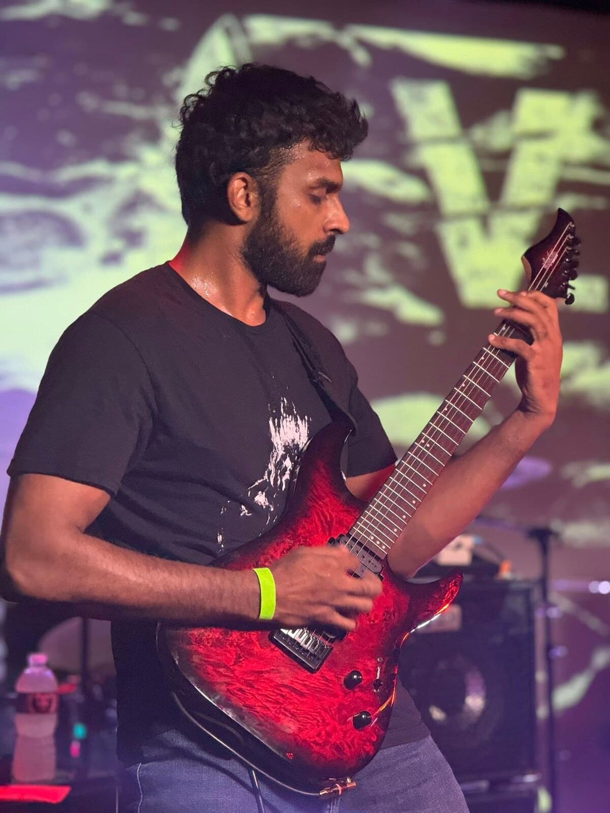 Krishna Peri performing on stage with his guitar under stage lighting